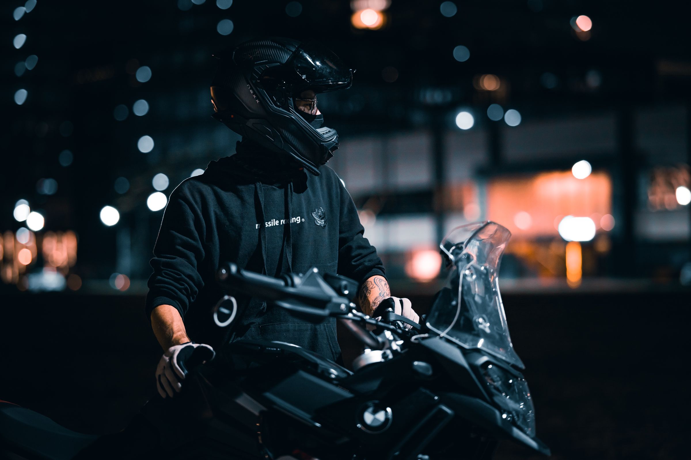 Motociclista à noite em via urbana com luzes desfocadas ao fundo